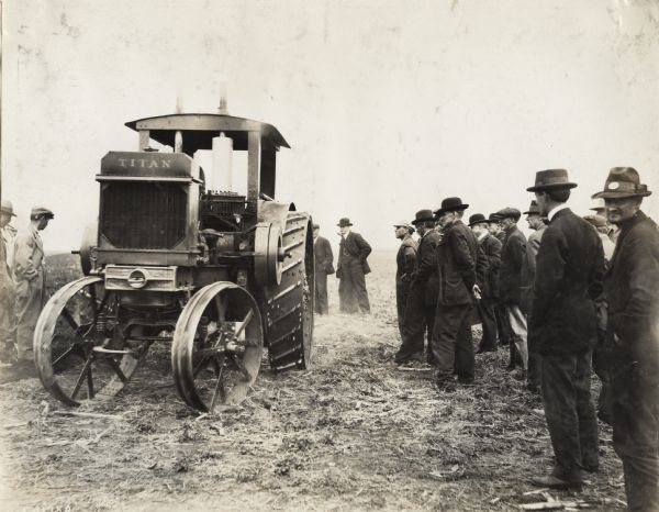 A group of men, probably farmers, inspect a Titan 15-30(?) tractor in a field.