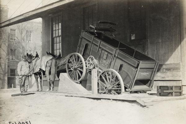 Man stands with horses as his Weber wagon is placed on wagon dump protected by the overhang of a building. Wagon dumps served to eliminate the task of unloading by hand.