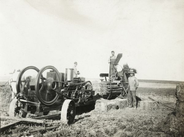 Men baling hay with engine powered hay press.