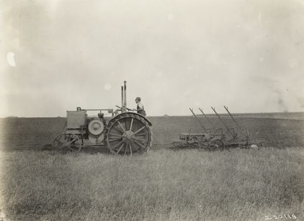 Side view of a farmer using an International 15-30 tractor to plow a field.