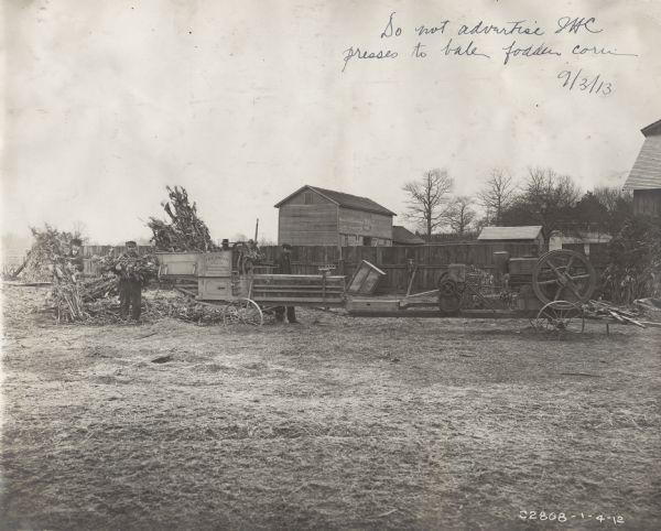 Men using an International Harvester stationary engine to power an IHC hay press to bale fodder.