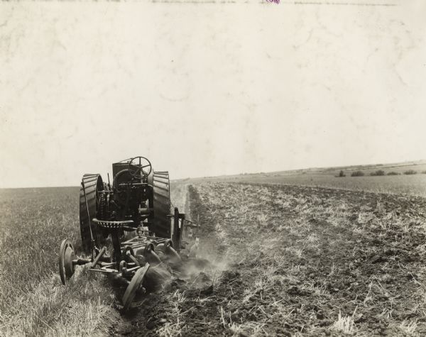 Rear view of a Mogul 8-16 tractor with a three bottom plow in a field.