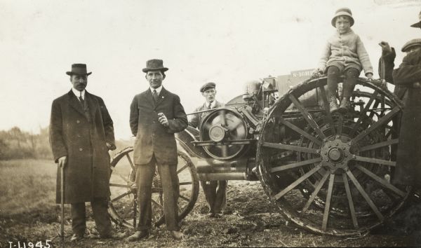 Group of several well-dressed men stand beside a Mogul 8-16 tractor, while a youth sits on top of a rear wheel.