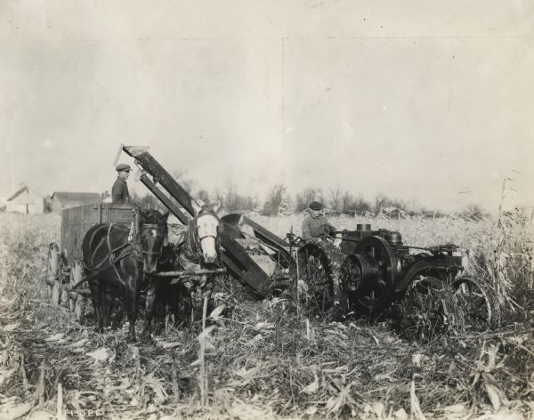 Men with a Mogul 8-16 tractor, corn picker and horse-drawn wagon in a cornfield.