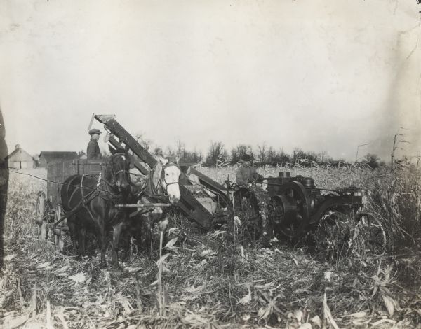Men with Mogul 8-16 tractor, corn picker(?) and wagon in a cornfield.
