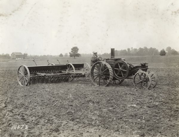 A man pulls grain drills through a field with a Mogul 8-16 tractor.