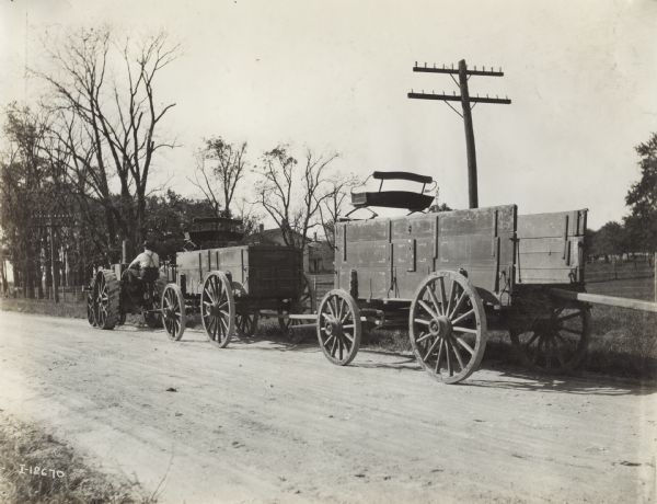 Man pulls two large wagons down a rural road with a Mogul 8-16 tractor.