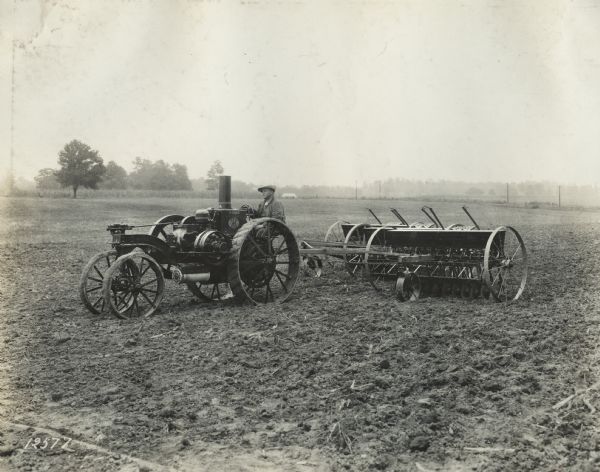Man pulls grain drills through a field with a Mogul 8-16 tractor.