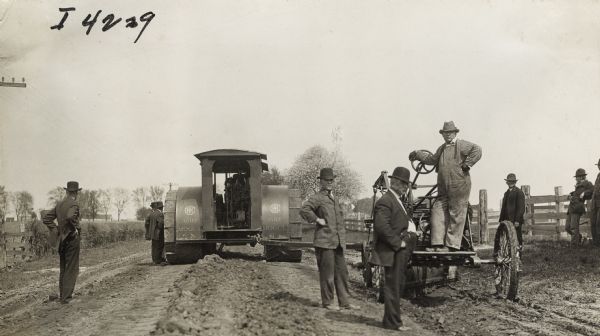 Group of men standing with road grader pulled by a 45 h.p. Mogul tractor along a rural road.