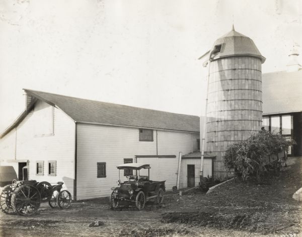 Mogul 8-16 tractor and International auto wagon parked outside silo and farm buildings.