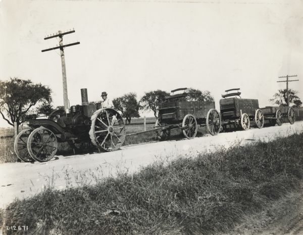Mogul 8-16 tractor pulling three farm wagons on a country road.