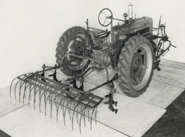 Studio shot of a No. 4 weeder mulcher attached to the rear of a Farmall H tractor. The equipment is shot against a white backdrop.