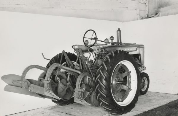 Farmall M tractor with an H&M direct-connected two way plow photographed against a white backdrop. The equipment may be experimental.