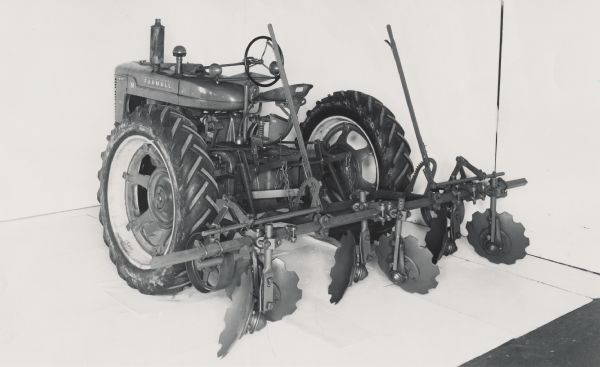 Farmall M tractor with mounted M-3 three row cane cultivator on display in front of a white backdrop. The equipment may be experimental.