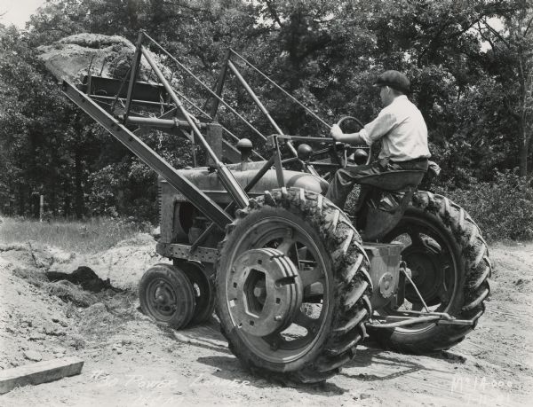 Man on tractor fitted with a #30 H&M power loader lifting soil.