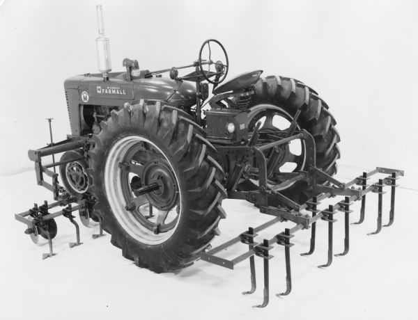 Farmall Super M tractor with a mounted HM 6-2 heavy duty vegetable cultivator on display in front of a white backdrop. The machinery may have been experimental.