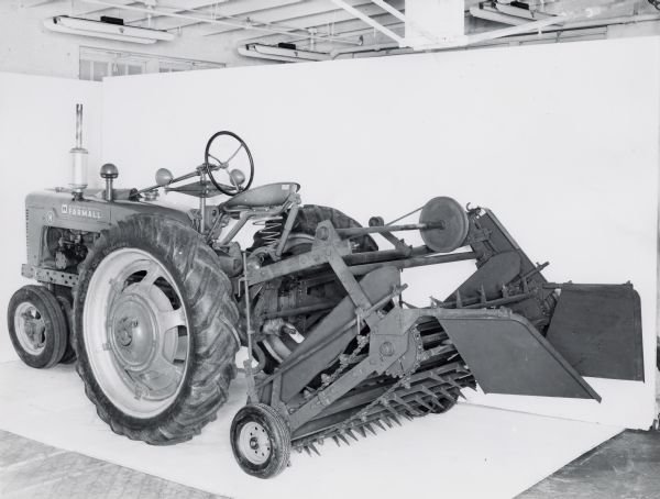 Farmall H tractor with a mounted HM peanut shaker on display in front of a white backdrop. The machinery may have been experimental.
