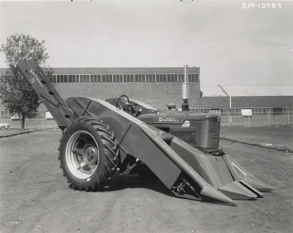 Model 192-M corn picker mounted on a Farmall Super M-TA tractor outside a large building.
