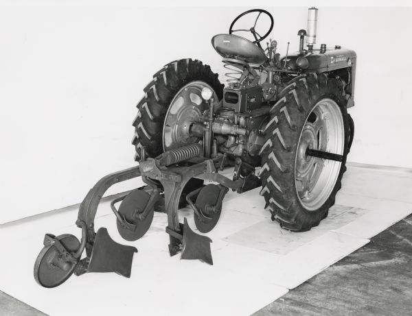 C-20 moldboard plow attached to a Farmall Super C tractor on display in front of a white backdrop. The equipment may be experimental.
