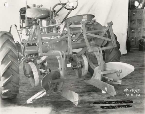 A&B hydraulic lift with No. 86 plow attached to a tractor on display in front of a white curtain backdrop. The equipment may be experimental.