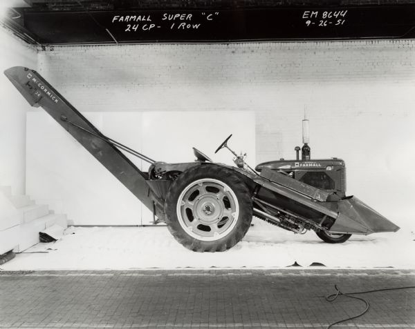 No. 24 corn picker mounted on a Farmall Super C tractor. In the background is a white wall for a backdrop.