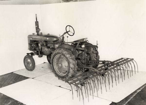 Three-quarter view from left rear of a No. 5 weeder mulcher attachment on a Farmall A tractor. The machinery was photographed against a white backdrop and may be experimental.