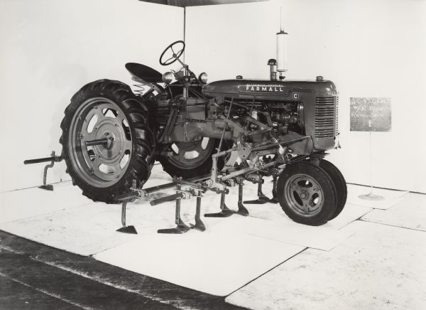 Engineering three-quarter view from right front of a Farmall C tractor with No. 452 cultivator and "R" type rear attachment. The equipment was photographed against a white backdrop and may be experimental.