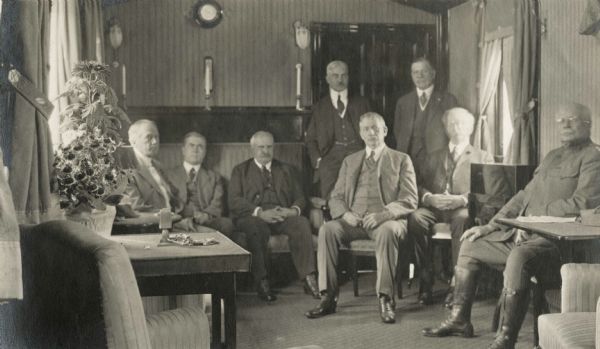 Group of Root Commission members sitting in "the drawing room car of the Imperial train of Ex-Czar Nicholas." Cyrus McCormick, Jr. is standing at right. The members are (left to right): Charles Edward Russell, Dr. John R. Mott, Rear Admiral James H. Glennon, Samuel R. Bertron, Senator Elihu Root, Cyrus H. McCormick, James Duncan, Major-General Hugh L. Scott.