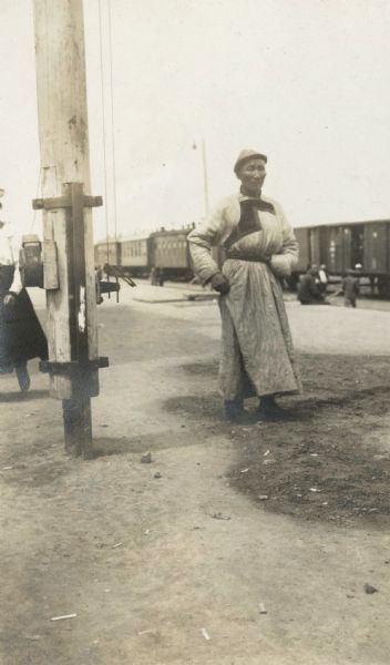 A man wearing a long coat belted at the waist, and a cap, is standing on a platform. The original caption identifies the man as a "Buryat prince." In the background is the Imperial train that carried members of the Root Commission.