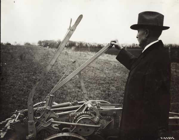 A man wearing a hat and overcoat is standing near a P&O plow with his hand on a lever.