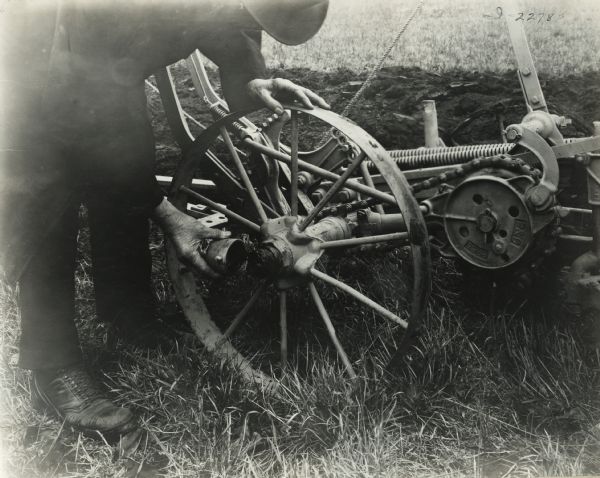 Close-up of a man wearing a hat bending over to remove a cap from the hub of a P&O tractor plow.