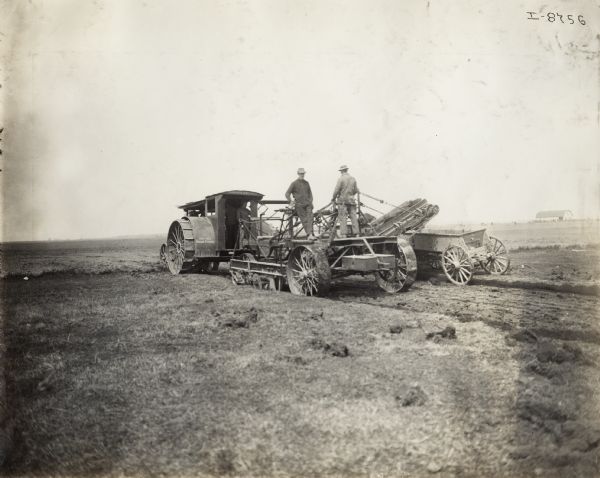 Rear view of a Mogul 30-60 tractor pulling an elevating grader. Two men stand on the platform of the grader while a wagon follows alongside to collect the stripped earth.