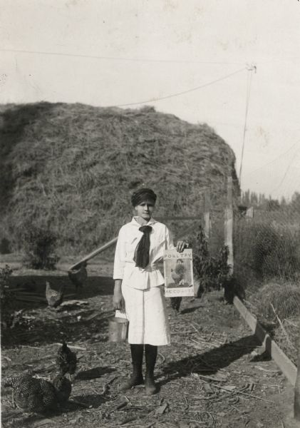 Mary Binegar, president of the Kiona-Benton School Poultry Club, holds a poultry account book as she stands outdoors near a haystack and several chickens at the Spokane Interstate Fair.