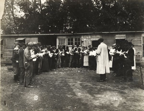 A group of individuals are gathered outdoors to examine chickens during a culling demonstration conducted by Professor Carrick of Purdue University.