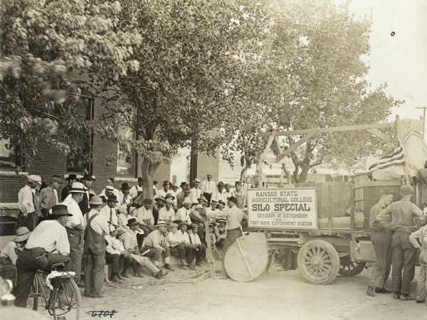 Group of men gathered around a truck with a large sign that reads, in part: "Kansas State Agricultural College Silo Special."