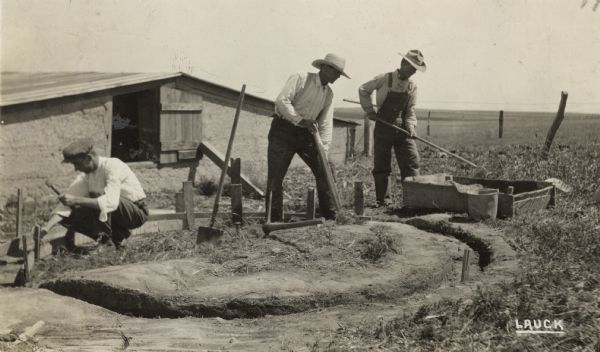 Three men breaking ground for a silo.