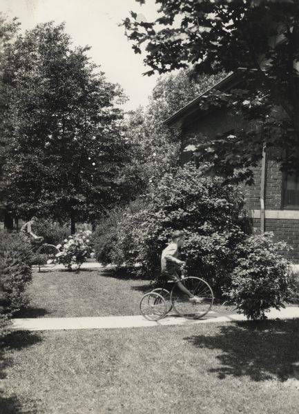 Two young boys ride bicycles (including a tricycle, or small "penny farthing") along the front walk toward the suburban residence of Robert Wallace, 10153 S. Hayne Street.