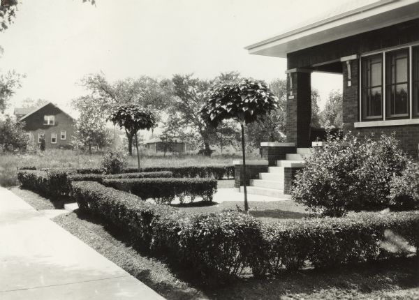 View from neighborhood sidewalk of suburban residence's front yard, outlined by low hedges.