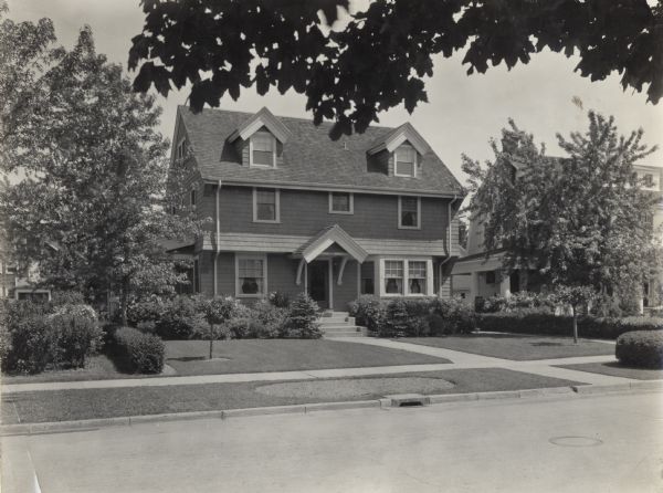 View from across street of the landscaping of a suburban home. Original title reads: "Good foundation plantings. Desirable open lawn evergreens may eventually become too large for their location."