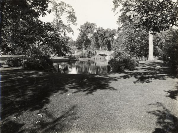 Elizabeth Park's landscaped park, including pond and footbridge. Two people sit on a bench in the shade on the right. The original caption describes the park as "well-landscaped."