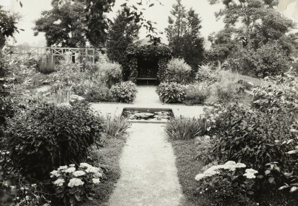 Formal garden with small pond, and in the background a vine-covered gazebo with a bench inside. Original caption reads: "Landscape — formal garden. 'Rydalmont'."