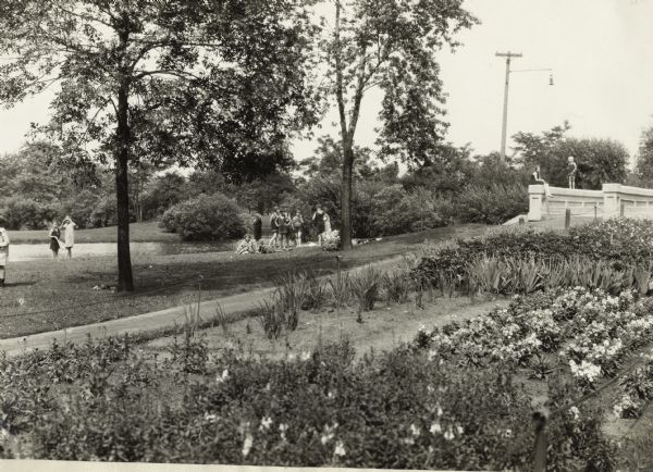 Children dressed in bathing suits at a small park with a swimming place. A garden is in the foreground.