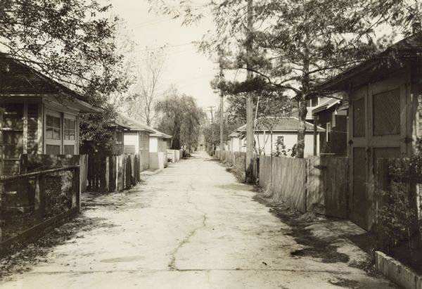 View down clean alley between the backs of houses in a residential neighborhood. Both sides of the alley are lined with garages.