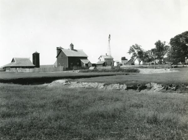 View of a washed and gullied field on the farm of LeRoy LeFevre. A farmhouse, barns, windmill, and other structures are in the background.