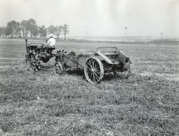 A man is using a Farmall Regular tractor and manure spreader to spread manure across a pasture at International Harvester's Hinsdale experimental farm.