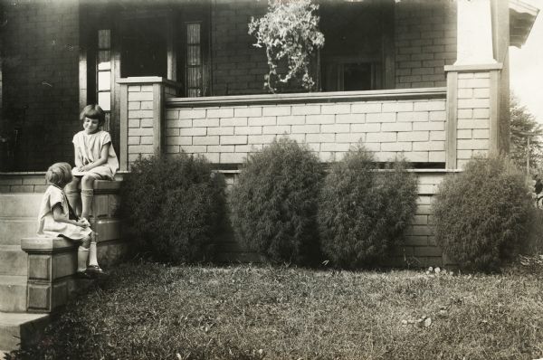 Two small girls seated on the front stoop of a house.