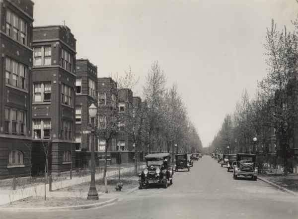 View down a tree-lined street of cars parked near 68th and Crandon Avenue. Identical apartment buildings are on both sides of the street.