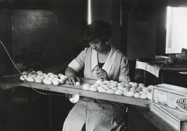 Helen Holden Besemer sitting in a wooden chair to candle eggs at Holden Poultry Farm.