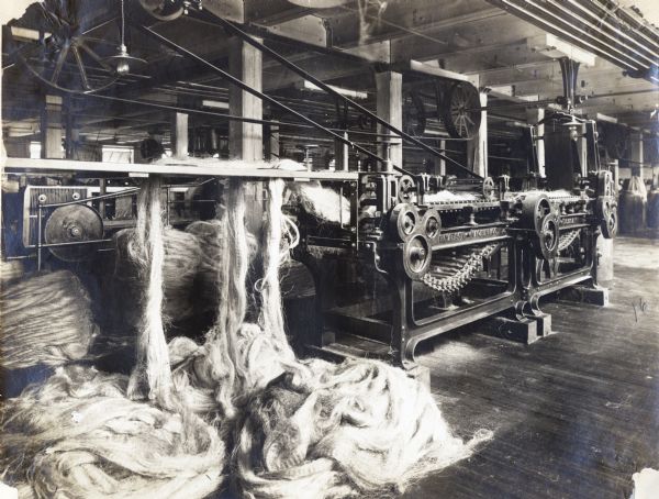 View of a spreading machine in an International Harvester twine mill, possibly at McCormick Works in Chicago. Fiber, possibly sisal, is piled on the floor around the machine.
