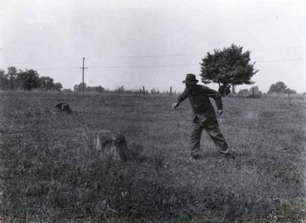 A man holding a metal instrument approaching a tree stump to inspect why a dynamite blast did not go off.